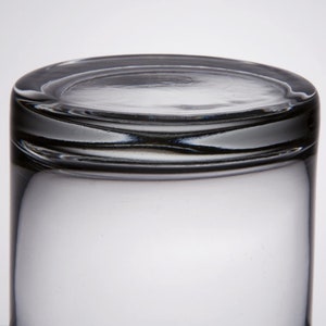 May include: A clear glass tumbler with a thick rim. The glass is empty and has a slight reflection of light.