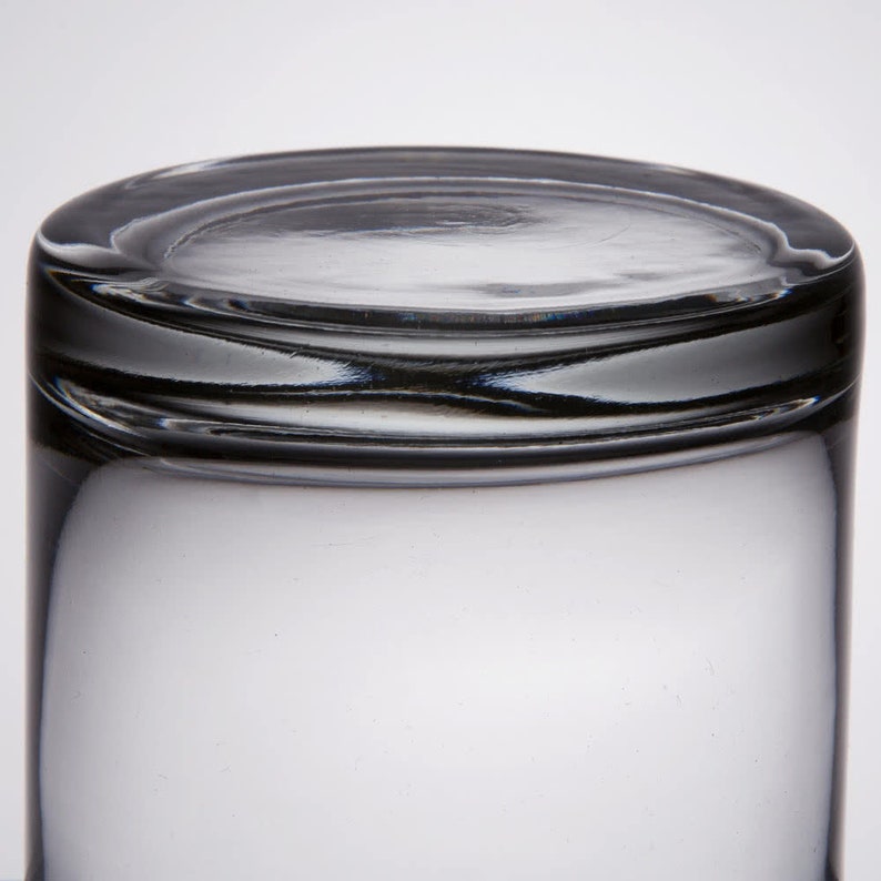 May include: A clear glass tumbler with a thick rim. The glass is empty and has a slight reflection of light.