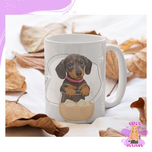 Puede incluir: Taza de cerámica blanca con una ilustración de cachorro de perro salchicha. El perro tiene pelaje marrón y negro y un collar rosa, que aparece en un vaso con cubitos de hielo. La taza tiene un asa blanca y un diseño de Kate's Designs.