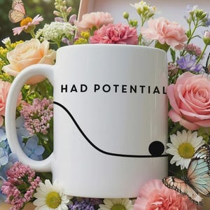 May include: White ceramic mug with the text "HAD POTENTIAL" in black, a curved line and a black dot. The mug is surrounded by a colourful arrangement of flowers and butterflies.