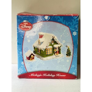 May include: A blue cardboard box featuring a graphic of Mickey's Holiday House, a green cabin with snow on the roof, a small dog house with a yellow dog, and a Christmas tree. The Disney logo is at the top, and the text Mickey's Holiday House is below.