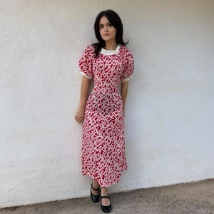 May include: A midi-length dress featuring a vibrant red background with a dense white floral pattern. The garment includes short puff sleeves, a rounded neckline with a white collar, and a fitted bodice that flows into a straight skirt.