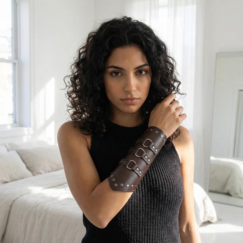 Pu&ograve; includere: Un bracciale in pelle marrone scuro con tre fibbie e rivetti argentati. Il bracciale &egrave; indossato sull'avambraccio. Un accessorio elegante in pelle marrone scuro.