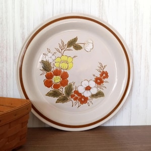 May include: A beige ceramic dinner plate with a brown rim and a floral design featuring red, yellow, and white flowers.