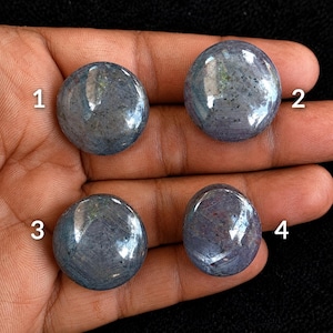 May include: Four round, polished blue-grey cabochon gemstones labelled with the numbers 1, 2, 3, and 4. Each stone features a smooth, domed surface with visible internal inclusions and a reflective lustre, showcasing varied shades of blue and grey.