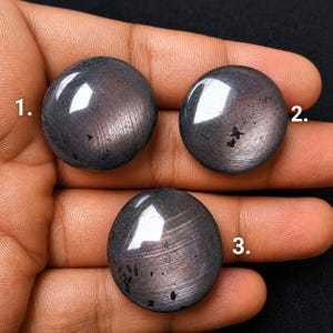 Peut inclure: Trois pierres précieuses rondes et polies de couleur gris foncé avec un éclat métallique et des textures de surface linéaires visibles. Chaque pierre est marquée d'un chiffre blanc, étiqueté 1, 2 et 3, indiquant des pièces distinctes.