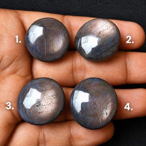 May include: Four round, polished cabochon gemstones with a dark, iridescent blue-grey surface and visible light reflections. Each stone is numbered 1 through 4 in white text, showcasing a smooth, domed shape and subtle metallic sheen.