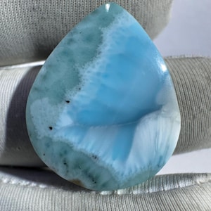 May include: A polished, teardrop-shaped gemstone with a striking blue and white pattern. The stone's surface has a glossy finish, with areas of light and dark blue, and white veining. The overall appearance is reminiscent of ocean waves.