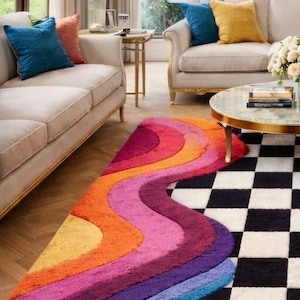 May include: A rectangular area rug featuring a split design. One half displays a vibrant, multi-colored pattern of wavy, curved stripes in shades of pink, orange, yellow, purple, and blue. The other half features a black and white checkerboard pattern.