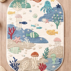 May include: An oval-shaped rug with a whimsical underwater scene. The rug features various sea creatures like fish, an octopus, and jellyfish, along with coral and seaweed. The color palette includes shades of blue, green, and beige, creating a playful and inviting design.