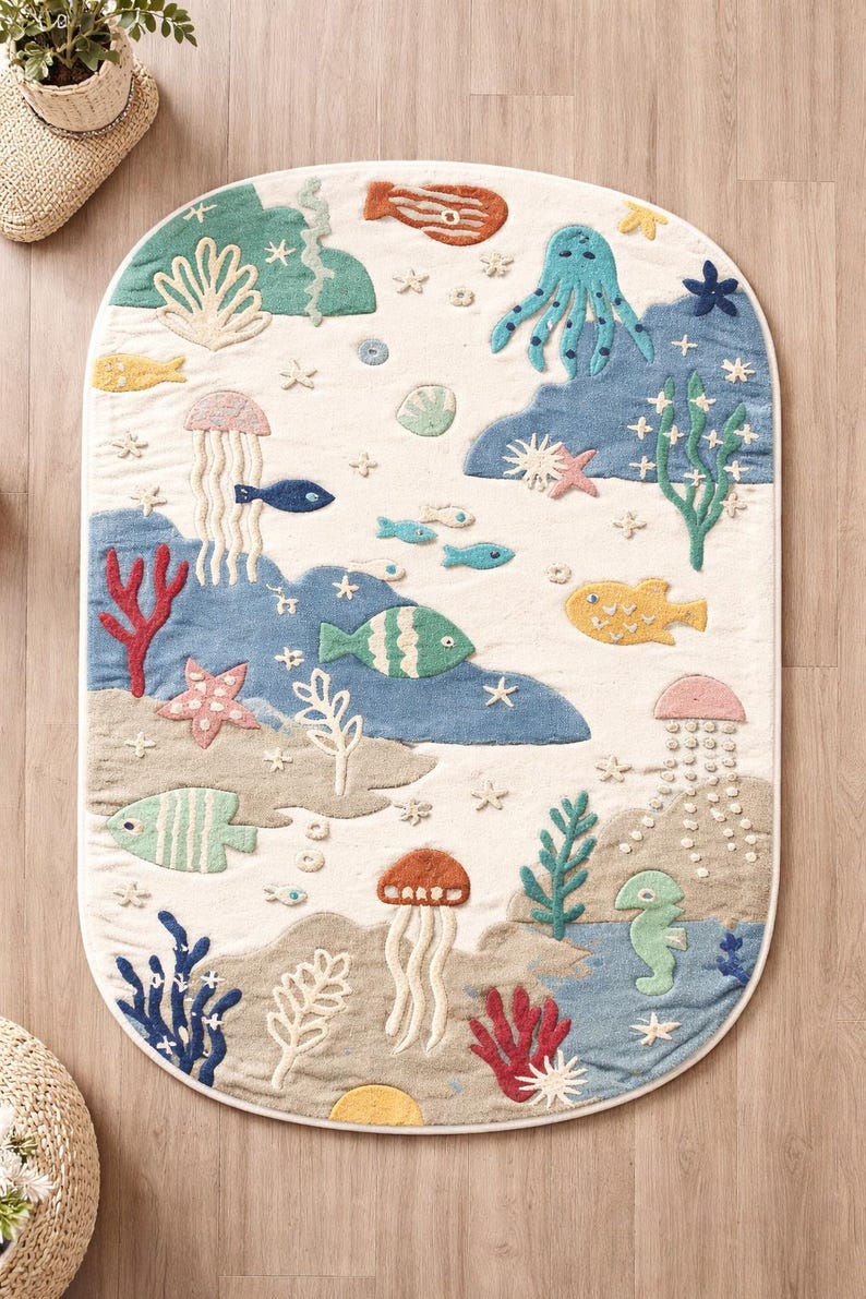 May include: An oval-shaped rug with a whimsical underwater scene. The rug features various sea creatures like fish, an octopus, and jellyfish, along with coral and seaweed. The color palette includes shades of blue, green, and beige, creating a playful and inviting design.
