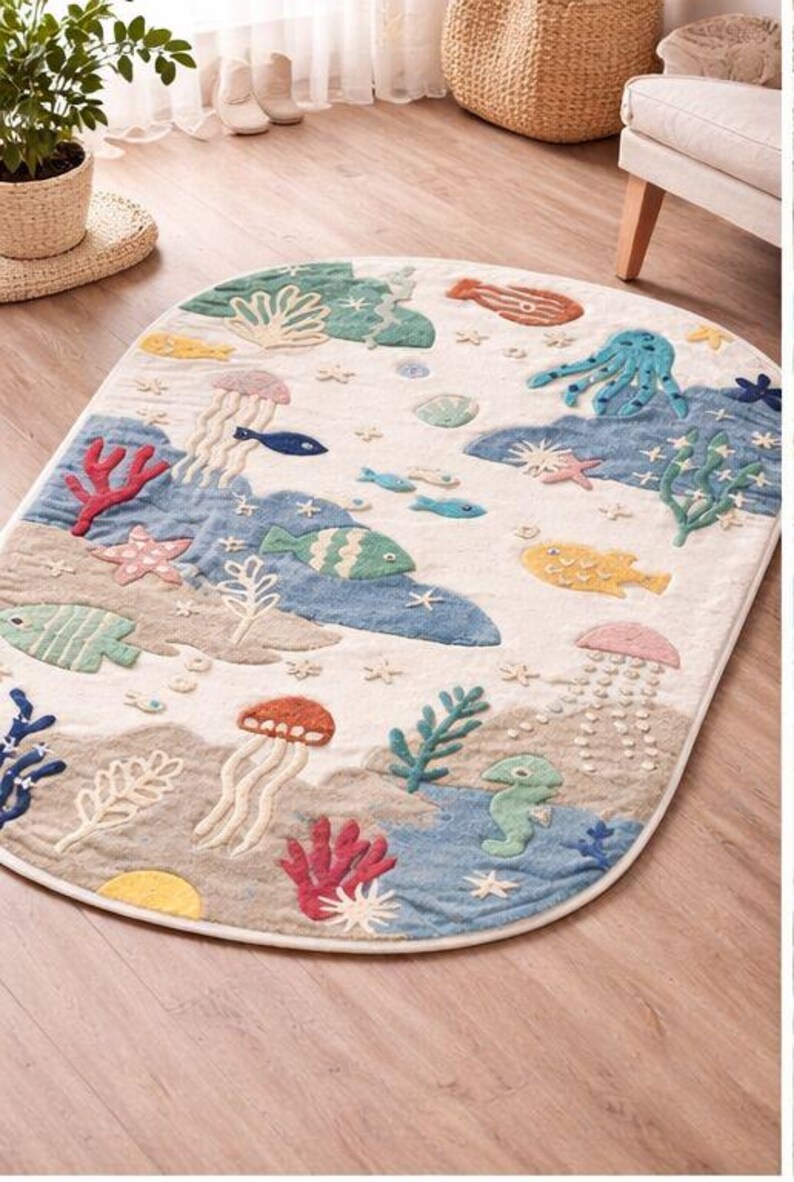 May include: An oval-shaped rug with a sea life design. The rug features colorful embroidered sea creatures, including fish, jellyfish, and an octopus, set against a cream-colored background with blue and beige accents. The rug is approximately 60 inches long.