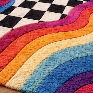 May include: A tufted area rug featuring a central black and white checkered pattern bordered by thick, wavy, multi-colored stripes in shades of magenta, orange, yellow, light blue, and purple, creating a vibrant and textured floor covering.