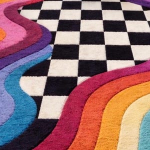 May include: A plush area rug featuring a central black and white checkered pattern flanked by thick, wavy, multi-colored bands in shades of orange, magenta, purple, light blue, and yellow, creating a textured, high-pile surface design.