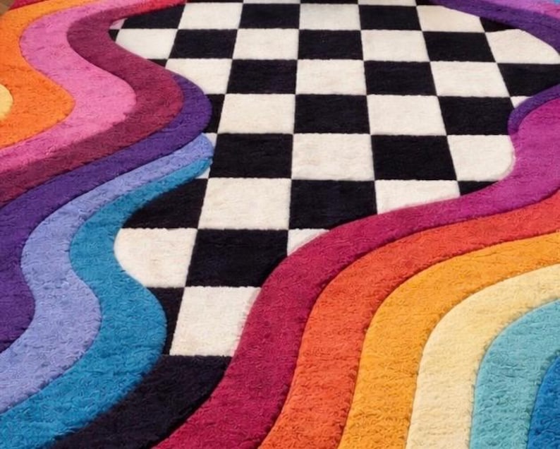 May include: A plush area rug featuring a central black and white checkered pattern flanked by thick, wavy, multi-colored bands in shades of orange, magenta, purple, light blue, and yellow, creating a textured, high-pile surface design.