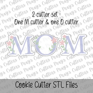 May include: A pair of cookie cutters forming the word "MOM". The letters are pale purple, decorated with pink and green floral designs. The image includes the text "2 cutter set: One M cutter & one O cutter" and "Cookie Cutter STL Files".