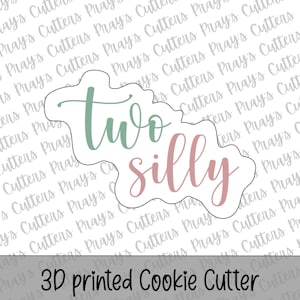 Può includere: Un tagliabiscotti stampato in 3D a forma di nuvola, con le parole "two silly" in corsivo. La parola "two" è in un verde tenue e "silly" in un rosa tenue. Il testo "3D printed Cookie Cutter" è in basso.