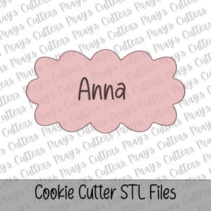 Può includere: Un tagliabiscotti rosa chiaro a forma di placca smerlata con il nome Anna scritto in corsivo marrone scuro al centro. Il design presenta uno sfondo con filigrana ripetuta e il testo Cookie Cutter STL Files nella parte inferiore.