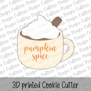 May include: A cream-colored cookie cutter shaped like a mug filled with a dark brown beverage, topped with white whipped cream and a brown cinnamon stick. The text "pumpkin spice" is printed in orange on the front of the mug.