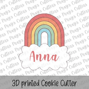 Puede incluir: Un cortador de galletas impreso en 3D con forma de arcoíris y nube. La nube tiene el nombre "Anna" en rosa. El arcoíris tiene arcos rojos, naranjas, amarillos, verdes y azules. El texto "3D printed Cookie Cutter" está en la parte inferior.