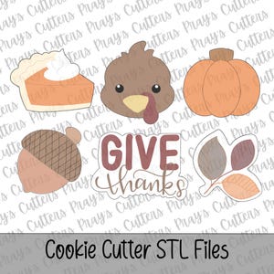 Könnte beinhalten: Ein Set aus sechs Ausstechformen zum Thema Thanksgiving, bestehend aus einem Stück Kürbiskuchen mit Schlagsahne, einem Truthahnkopf, einem runden Kürbis, einer Eichel, einem Schild mit dem Text GIVE THANKS und drei herbstlichen Blättern.