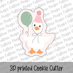 Può includere: Un tagliabiscotti stampato in 3D a forma di oca dei cartoni animati con cappello da festa e palloncino. L'oca è bianca con zampe arancioni e un fiocco. Il testo "3D printed Cookie Cutter" è in basso.