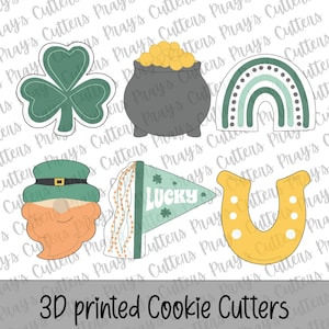Puede incluir: Un conjunto de cortadores de galletas impresos en 3D con símbolos del Día de San Patricio. Incluye un trébol, una olla de oro, un arcoíris, un duende, una bandera con el texto "LUCKY" y una herradura. El texto "3D printed Cookie Cutters" está en la parte inferior.