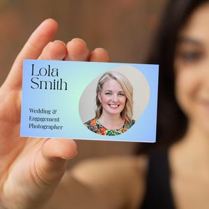 Könnte beinhalten: Eine Visitenkarte, die von einer Person gehalten wird. Die Karte zeigt den Namen "Lola Smith" und den Titel "Wedding & Engagement Photographer". Ein Porträt einer Frau mit blonden Haaren und einem floralen Oberteil ist ebenfalls auf der Karte abgebildet. Der Hintergrund der Karte ist hellblau.