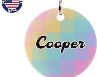 May include: A round pet tag with a pastel checkered pattern in shades of yellow, green, blue, and pink. The name "Cooper" is written in a black, cursive font. A metal ring is attached at the top. The tag has a "Made in the USA" logo.
