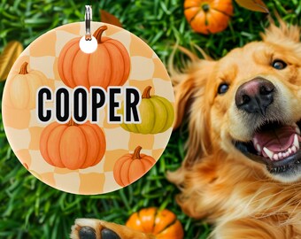 May include: A round, cream-colored pet tag with the name "COOPER" in bold black letters, surrounded by orange pumpkins on a checkered background. A happy golden retriever dog is lying on green grass, with pumpkins scattered around.