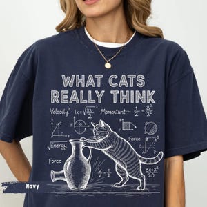 Könnte beinhalten: Marineblaues T-Shirt mit dem weißen Text "WHAT CATS REALLY THINK". Die Illustration zeigt eine Katze und mathematische Gleichungen. Ein lässiger, bequemer Stil.