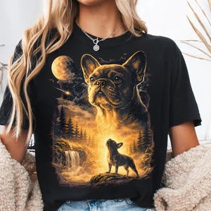 May include: Black t-shirt featuring a detailed illustration of a French Bulldog. The artwork includes a night sky with a moon, stars, and a waterfall scene. The dog is depicted in a golden, glowing light.