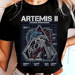 Op de afbeelding: Zwart T-shirt met een gedetailleerde afbeelding van de Artemis II-missie. Het ontwerp bevat technische specificaties, een diagram van het maanoppervlak en de namen Wiseman, Glover, Koch en Hansen. Het shirt heeft een ronde hals.