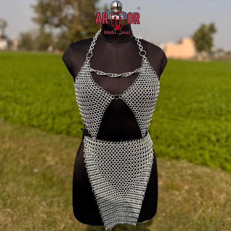 A front view of the complete silver chainmail dress set on a black dress form in an outdoor grassy setting.