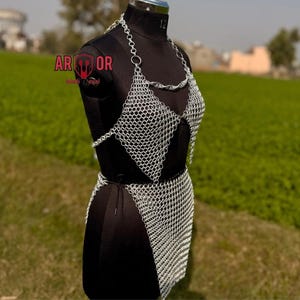 A three-quarter front view of the silver chainmail top and skirt on a black dress form outdoors with a green field background.