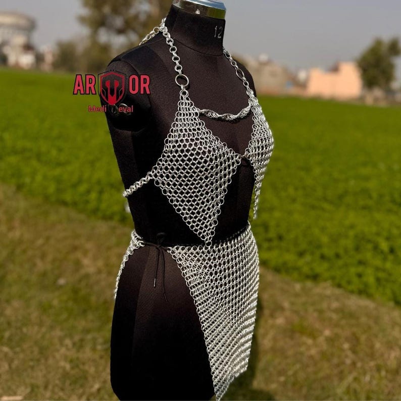 A three-quarter front view of the silver chainmail top and skirt on a black dress form outdoors with a green field background.