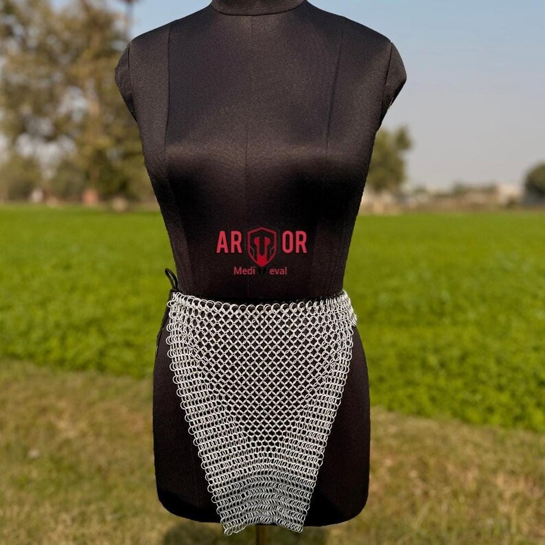 A view of only the silver chainmail skirt worn on the lower half of a black dress form outdoors.