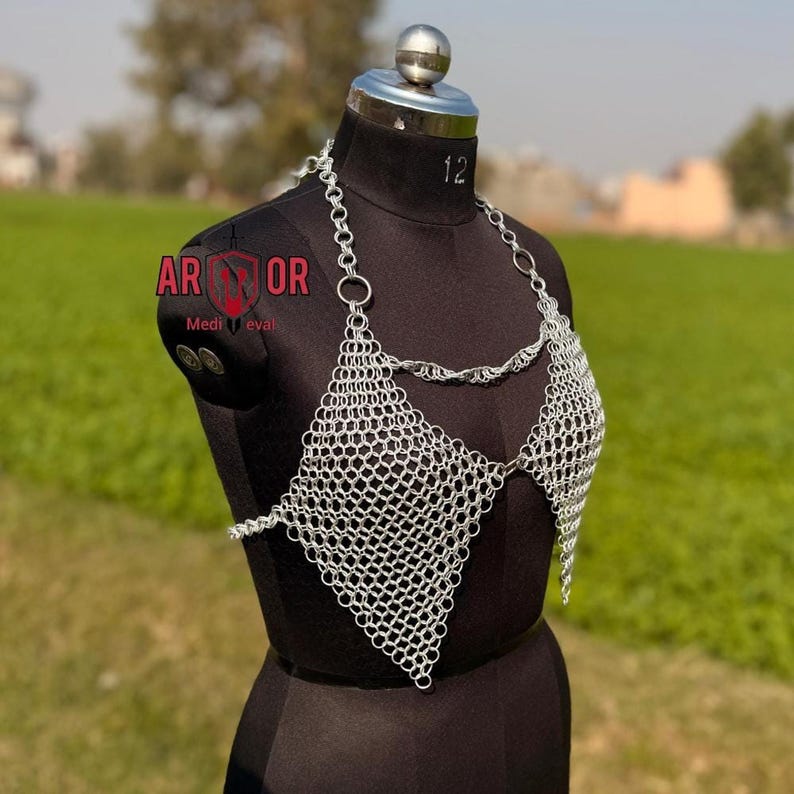 A close-up front view of the triangular silver chainmail halter top on a black dress form outdoors.