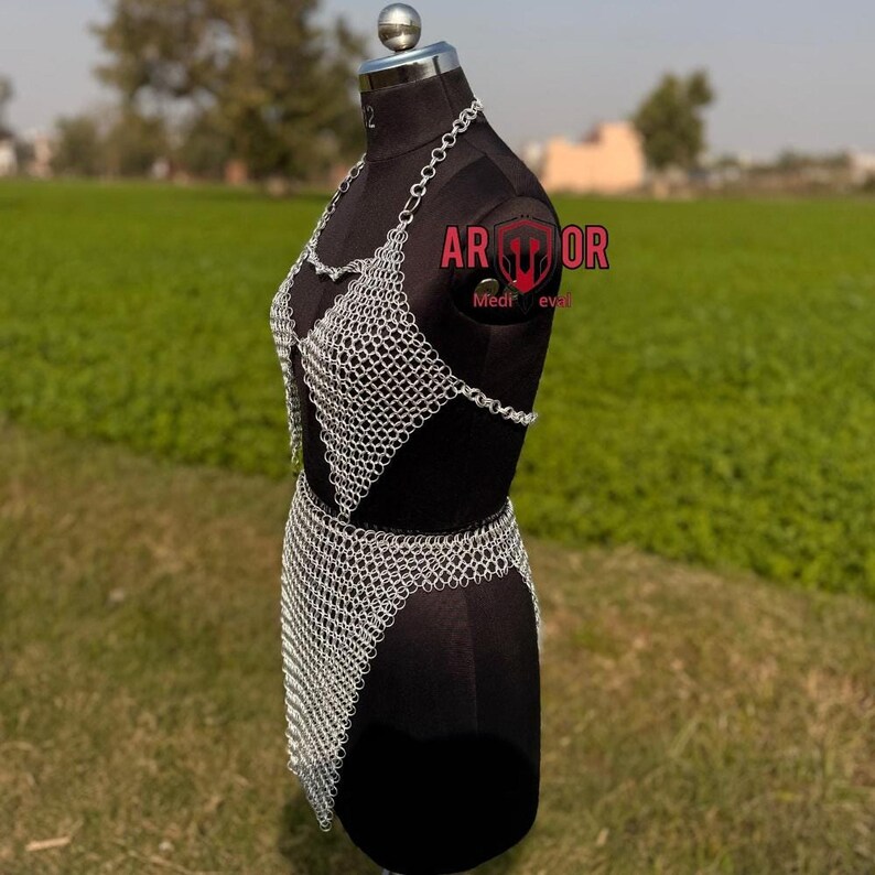 A side angle of the complete silver chainmail outfit on a black dress form against an outdoor field.
