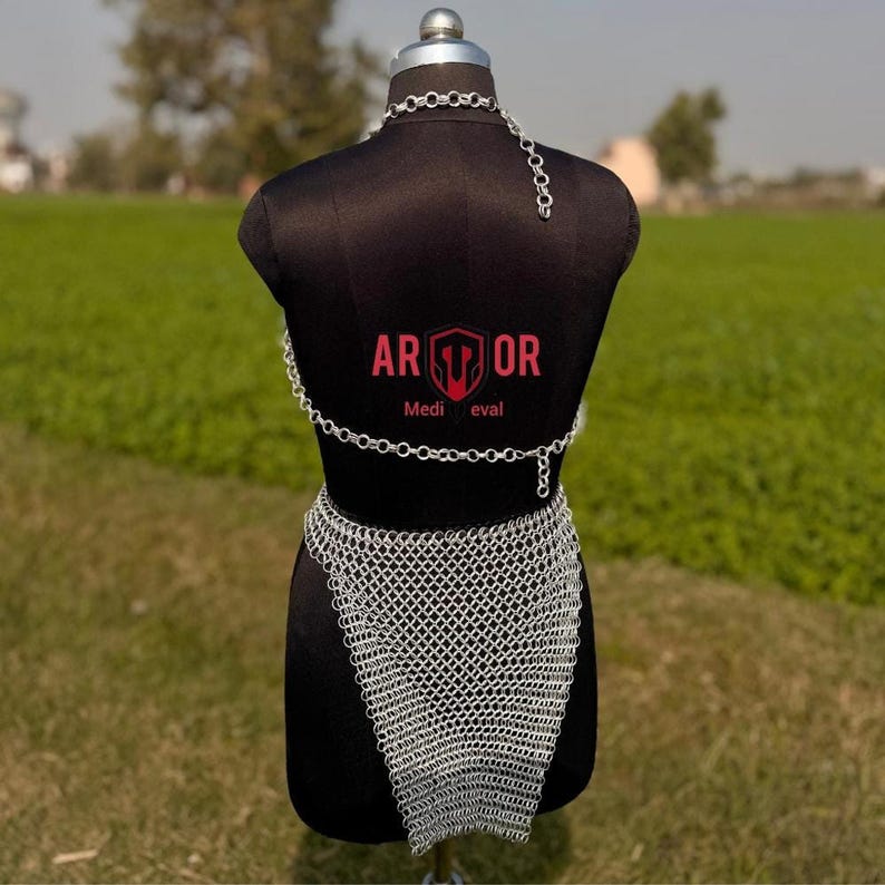 A rear view of the complete silver chainmail skirt and top set on a black mannequin outdoors.
