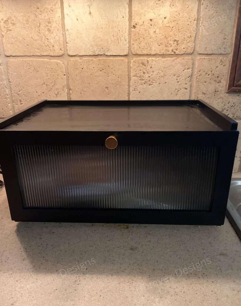 May include: A black cabinet with a ribbed glass door and a gold-colored knob. The cabinet is rectangular and sits on a countertop. The background features a tiled wall.