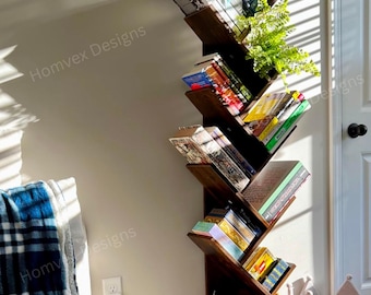 May include: A dark brown, tree-shaped bookshelf filled with books and a small plant. The bookshelf has a unique zig-zag design and sits against a light-colored wall. The top shelf displays the text "MY ROMANCE."