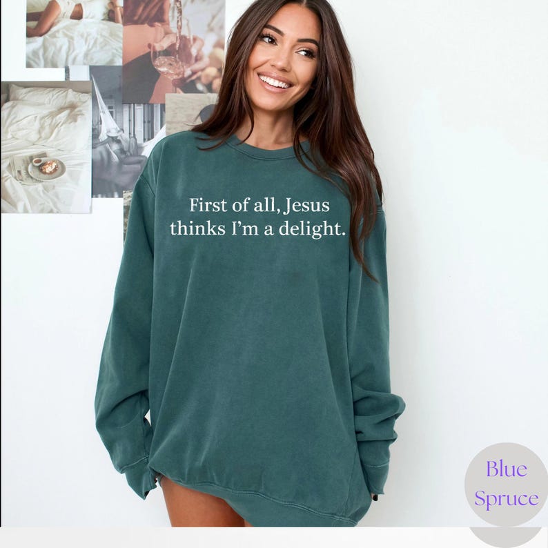May include: Teal-colored sweatshirt with the text "First of all, Jesus thinks I'm a delight." The sweatshirt has long sleeves and a crew neck. The brand name "Blue Spruce" is in a circle on the bottom right.
