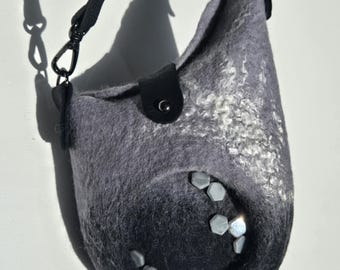 May include: A gray and black felt crossbody bag with a black strap and clasp. The bag has a rounded shape with a flap closure and decorative geometric accents. The bag's color fades from gray to black.