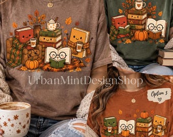 May include: Three t-shirts featuring autumn-themed illustrations of anthropomorphic books, pumpkins, and mugs of hot beverages. The designs include stacks of books with faces, reading glasses, and falling leaves in warm seasonal colors on brown, green, and orange fabric.