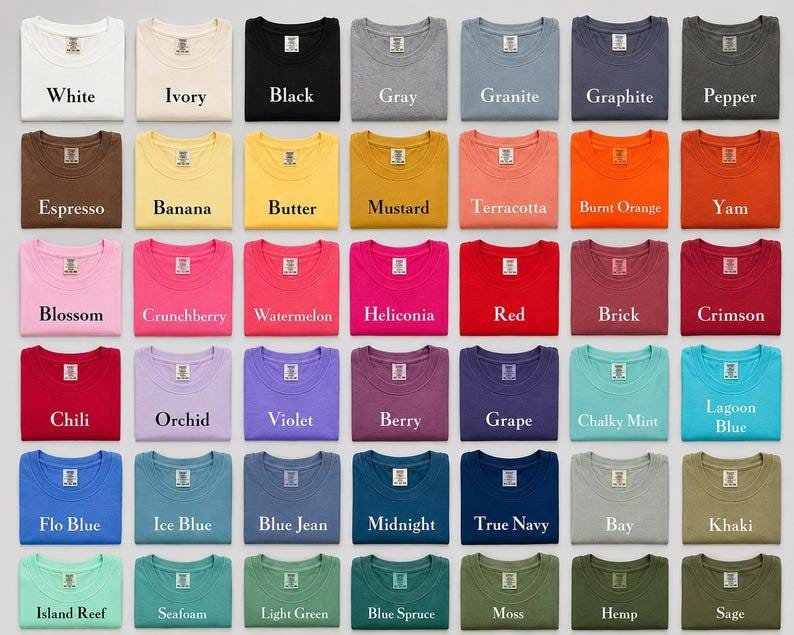 May include: A grid of forty-nine folded crew neck t-shirts in various solid colours, each labelled with its specific colour name including White, Ivory, Black, Gray, Granite, Graphite, Pepper, Espresso, Banana, Butter, Mustard, Terracotta, Burnt Orange, Yam, Blossom, Crunchberry, Watermelon, Heliconia, Red, Brick, Crimson, Chili, Orchid, Violet, Berry, Grape, Chalky Mint, Lagoon Blue, Flo Blue, Ice Blue, Blue Jean, Midnight, True Navy, Bay, Khaki, Island Reef, Seafoam, Light Green, Blue Spruce, Moss, Hemp, and Sage.