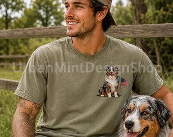 May include: An olive green short-sleeve crew neck t-shirt featuring a graphic print on the left chest of an Australian Shepherd dog sitting next to a small American flag. The shirt has a relaxed fit and a solid, muted color throughout the fabric.