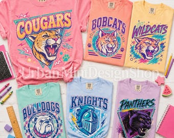May include: Six short-sleeve t-shirts in pink, peach, yellow, mint, light blue, and lavender. Each shirt features a graphic print of a mascot, including a cougar, bobcat, wildcat, bulldog, knight, and panther, with corresponding team names.