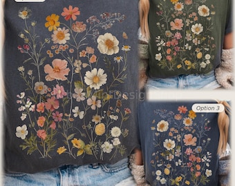 May include: Three t-shirts featuring floral prints. Option 1 is a dark gray shirt with a large wildflower graphic. Option 2 is an olive green shirt with a similar floral design. Option 3 is a blue shirt with a smaller wildflower graphic.