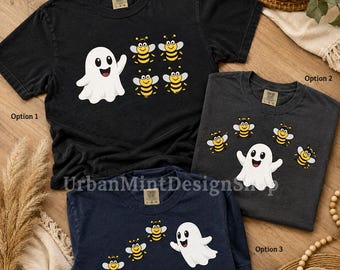May include: Three short-sleeve t-shirts in black, charcoal, and navy blue. Each shirt features a graphic of a white ghost and several yellow and black striped bees. The shirts have a crew neckline and a tag at the inner collar. Text reads: Want custom text or image? Message us!